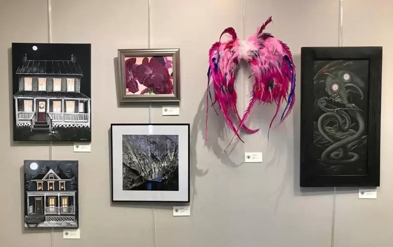 Photo of art hanging on wall including houses, abstract, alien, and feather fairy wings.